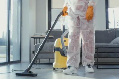 Worker in white coveralls and orange gloves vacuuming a living room