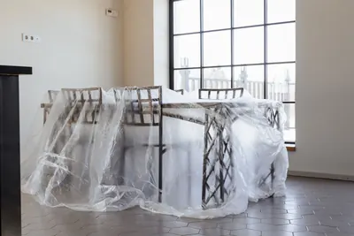 Table and chairs covered in clear plastic sheeting in a bright room
